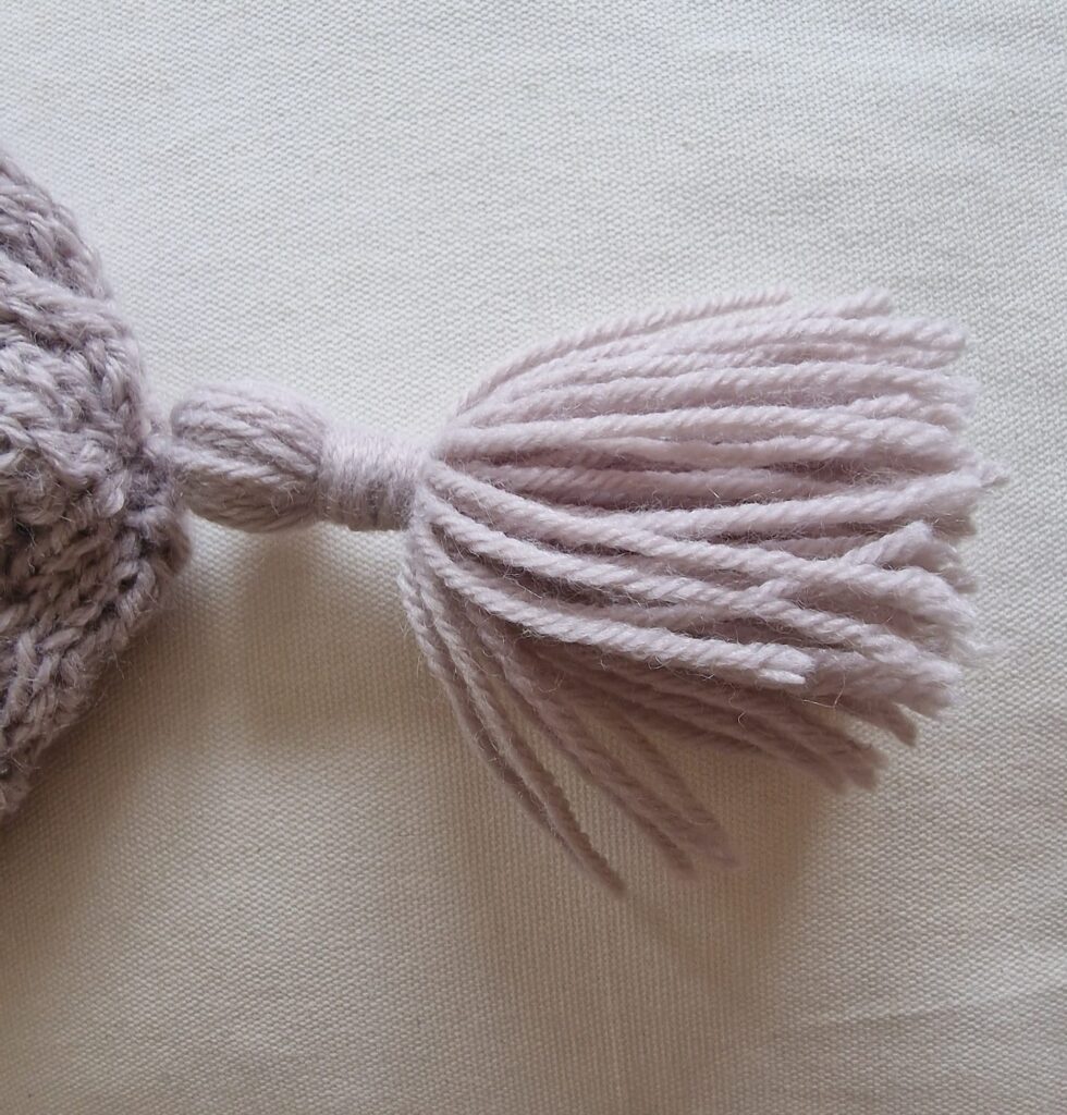 View of tassel on knitted beanie with Aran stitch panel