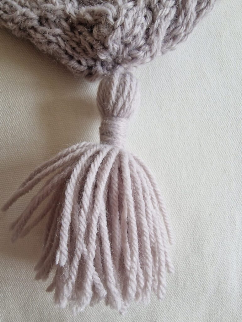 View of tassel on knitted beanie with Aran stitch panel